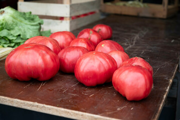 A group of large, beautiful tomatoes rests on a wooden surface in the market in soft sunlight