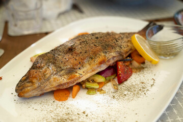 Baked trout fish, served on a white plate with fresh salad and cooked barley