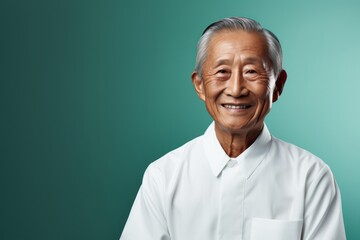 Fototapeta premium Portrait of a blissful asian elderly 100 years old man wearing a classic white shirt against a soft teal background. AI Generation