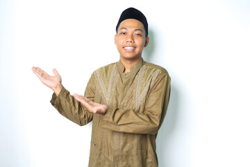 smiling asian muslim man wearing islamic dress presenting empty space isolated on white background