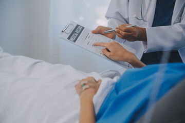 The senior woman specialist doctor with stethoscope checking up happy young Asian female patient lying in bed with receiving an intravenous saline drip in recovery room. Healthcare, medical insurance.