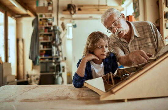 Grandfather and grandson working on a model boat in a woodworking workshop