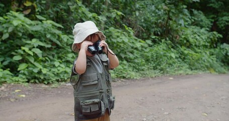 An adventurous child dressed in explorer gear uses binoculars in a lush green forest