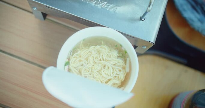 Overhead view of instant noodles being prepared with steaming hot water poured from an electric kettle, Hot water pouring into a cup of instant noodles, a quick meal preparation