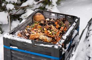 Showing open compost bin with bio waste inside, outdoors in the winter, snowy cold weather.
