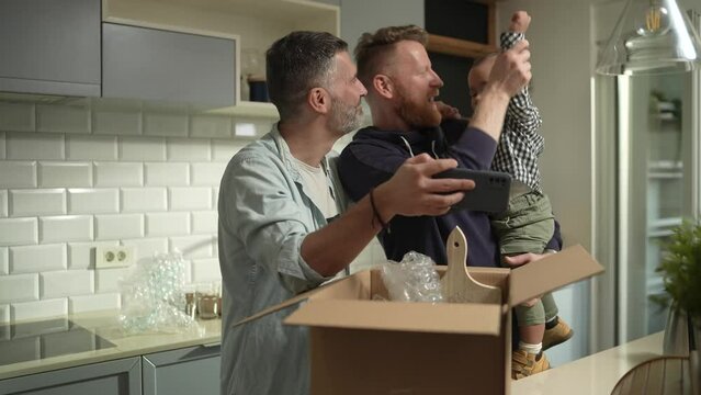 Gay couple taking selfie with toddler in kitchen during unpacking