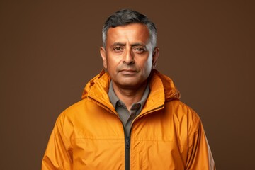 Obraz premium Portrait of a satisfied indian man in his 50s wearing a lightweight packable anorak against a soft brown background. AI Generation