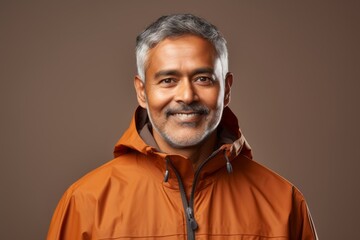 Fototapeta premium Portrait of a satisfied indian man in his 50s wearing a lightweight packable anorak against a soft brown background. AI Generation