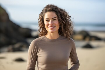 Portrait of a satisfied woman in her 30s showing off a thermal merino wool top against a sandy beach background. AI Generation
