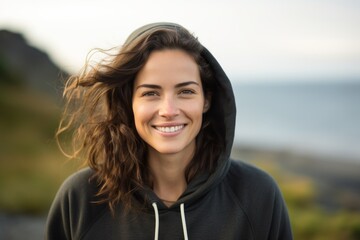 Portrait of a smiling woman in her 30s sporting a comfortable hoodie against a serene seaside background. AI Generation - Powered by Adobe