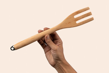 Hand holding wooden fork on light peach background.