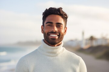 Portrait of a grinning indian man in his 20s wearing a classic turtleneck sweater against a serene seaside background. AI Generation