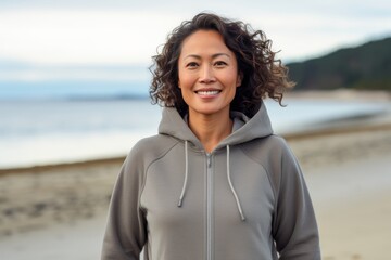 Portrait of a happy asian woman in her 40s wearing a zip-up fleece hoodie against a peaceful tide pool background. AI Generation