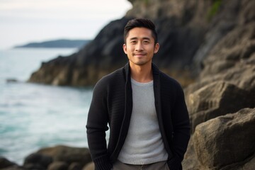 Fototapeta na wymiar Portrait of a satisfied asian man in his 30s wearing a chic cardigan against a rocky shoreline background. AI Generation