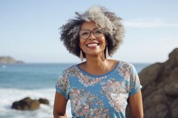 Portrait of a jovial afro-american woman in her 60s dressed in a casual t-shirt against a rocky shoreline background. AI Generation