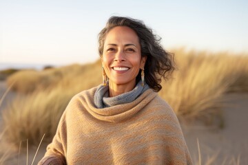 Portrait of a smiling indian woman in her 50s wearing a cozy sweater against a serene dune...