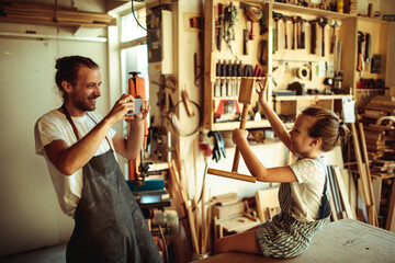 Father teaching daughter woodworking in workshop - obrazy, fototapety, plakaty