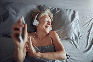 Happy senior woman listening and enjoying relaxing music in bed - Powered by Adobe