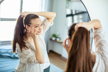 Woman styling her ponytail in the mirror at home - obrazy, fototapety, plakaty