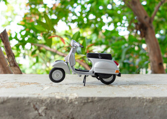 Miniature classic scooter on the cement floor with nature background. After some edits.