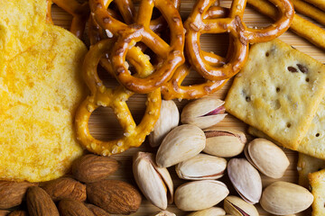 Close up of Almonds, pistachios, Crackers, potato chips and mini pretzels. Assortment of crispy appetizers. Wooden plate with Salty snacks. Party mix. top view