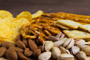 roasted peanuts on a table. Close up of Almonds, pistachios, Crackers, potato chips and mini pretzels. Assortment of crispy appetizers. Wooden plate with Salty snacks. Party mix.