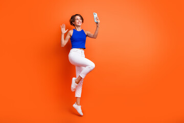 Full length portrait of crazy person jump hold smart phone make selfie arm waving hi empty space...