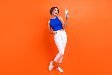 Full length portrait of lovely positive person use smart phone chatting isolated on vibrant orange color background