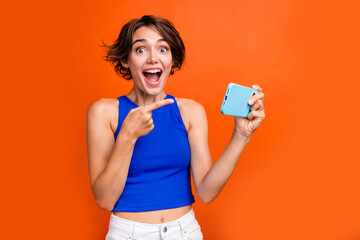 Photo of impressed cute person open mouth direct finger arm hold smart phone isolated on orange color background