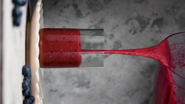 Berry smoothie, pouring fresh blueberry, raspberry, strawberry smoothie in a glass, vertical