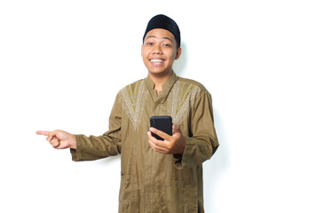 excited asian muslim male holding mobile phone and pointing to beside isolated on white background