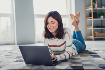 Full size photo of cute cheerful girl laying carpet floor use wireless laptop typing email living room house inside