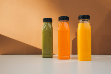 Fruit and vegetable smoothies in transparent plastic bottles. Green, orange smoothies on a brown-white background. The concept of healthy eating. Front view