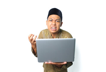 asian muslim man holding laptop with angry expression wearing islamic dress isolated on white background
