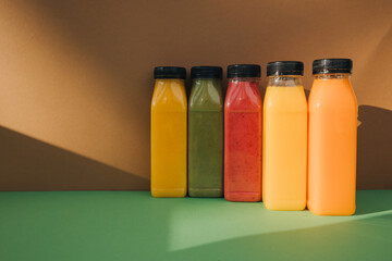 Fruit and vegetable smoothies in transparent plastic bottles. Red, green, orange smoothies on a brown-green background. The concept of healthy eating. Front view