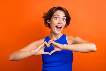 Photo of adorable excited girl dressed blue top open mouth showing arms heart isolated orange color background