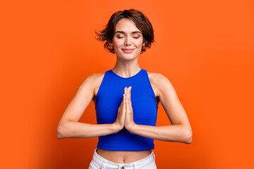 Photo of dreamy adorable girl dressed blue top closed eyes arms together closed eyes isolated orange color background