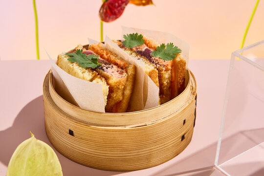 Asian sando sandwich with tuna and spicy sauce, presented in a bamboo steamer amidst abstract floral art