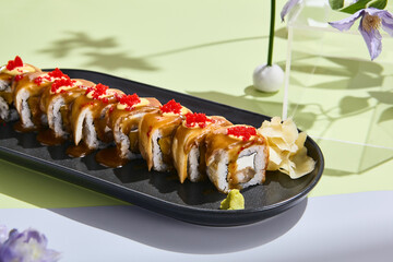 Summery sushi concept with eel roll, tobiko caviar, and unagi sauce amidst pastel floral decor