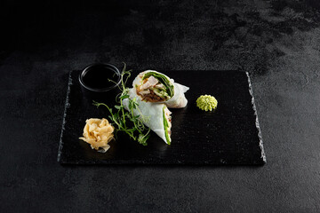 Fototapeta na wymiar Chicken and wood mushroom sprint roll in rice paper with pea sprouts on a black slate