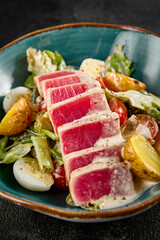 Seared medium-rare tuna Salad Nicoise, with potatoes, greens, and eggs in a teal bowl