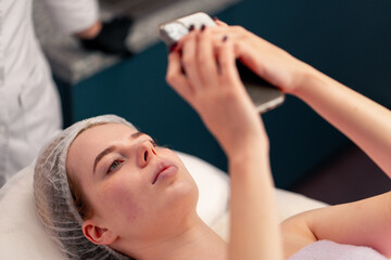 girl lying on a couch in a beauty salon taking a photo of her face after a cosmetic procedure