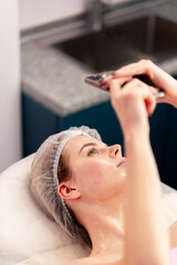 Fototapeta premium a girl lies on sofa in beauty salon taking a photo of her face with gel during a cosmetic procedure