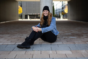 Red-haired woman with black jeans, black sweater and denim jacket in an urban location.