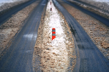 Asphalt  roadway covered with slushy snow and orange plastic pole with reflectors to separate lanes of cars for ensure traffic safety. Slush on winter road, snowy unplowed road. Selective focus