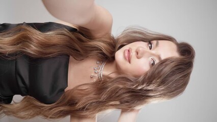 An elegantly dressed girl with evening makeup, hairstyle and jewelry makes a vertical video on her phone's selfie camera. A young woman take a selfie with the front camera of her smartphone. - Powered by Adobe