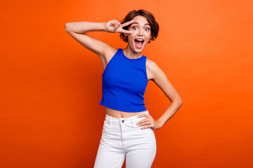 Photo of impressed funky lady wear blue singlet open mouth showing v-sign cover eyes isolated orange color background