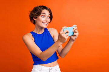 Portrait of funky nervous person biting lips hold smart phone playing games isolated on orange color background