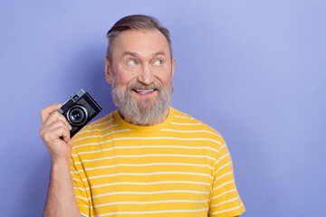 Photo of pleasant positive senior man dressed striped t-shirt hold camera look at sale empty space isolated on purple color background