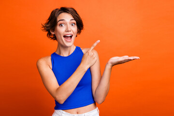 Photo of excited funky lady wear blue singlet showing finger arm empty space isolated orange color background
